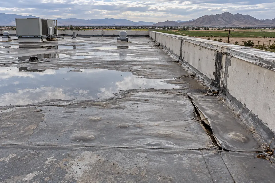 Split membrane seam and standing water beside a parapet wall on a flat roof