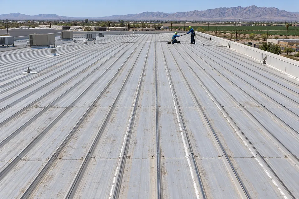 Long ribbed metal roof on a commercial building with two roofers working on fasteners